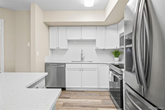 kitchen with white cabinets, appliances with stainless steel finishes, light stone countertops, and sink