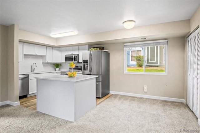 kitchen featuring decorative backsplash, appliances with stainless steel finishes, light carpet, a kitchen island, and white cabinetry