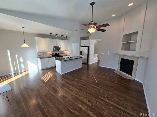 kitchen featuring white cabinets, dark countertops, appliances with stainless steel finishes, open floor plan, and a fireplace