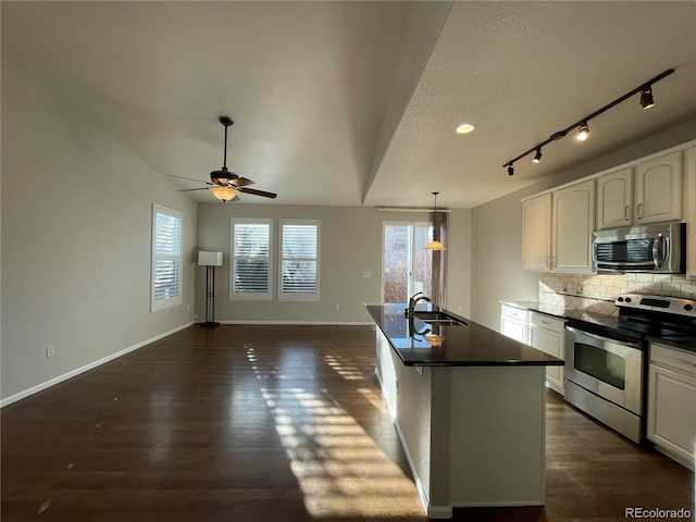 kitchen featuring stainless steel appliances, a sink, decorative backsplash, dark wood-style floors, and dark countertops