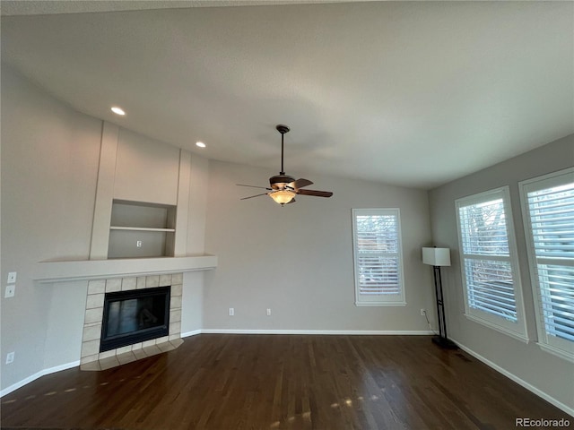 unfurnished living room with dark wood finished floors, lofted ceiling, a ceiling fan, a tile fireplace, and baseboards