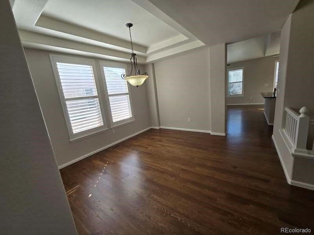 unfurnished dining area with baseboards, a tray ceiling, and wood finished floors