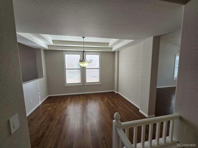 empty room with baseboards, a textured ceiling, a tray ceiling, and wood finished floors