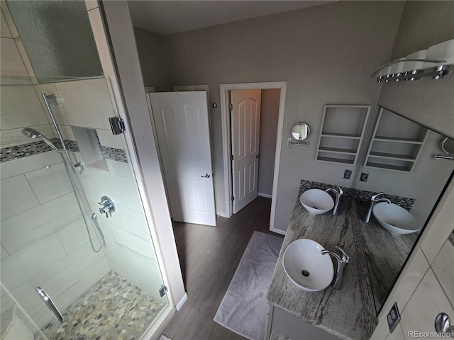 bathroom with double vanity, a sink, a shower stall, wood finished floors, and baseboards