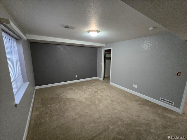 carpeted empty room featuring a textured ceiling, visible vents, and baseboards