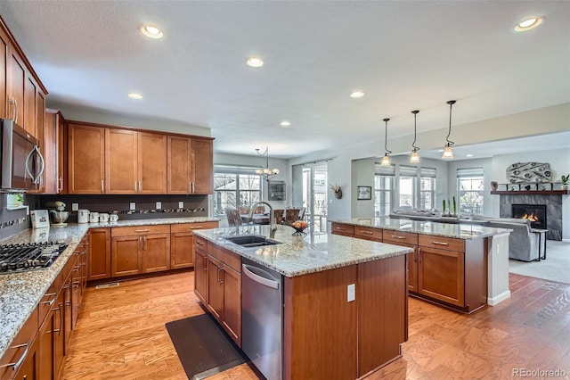 kitchen with sink, hanging light fixtures, a center island with sink, appliances with stainless steel finishes, and light wood-type flooring