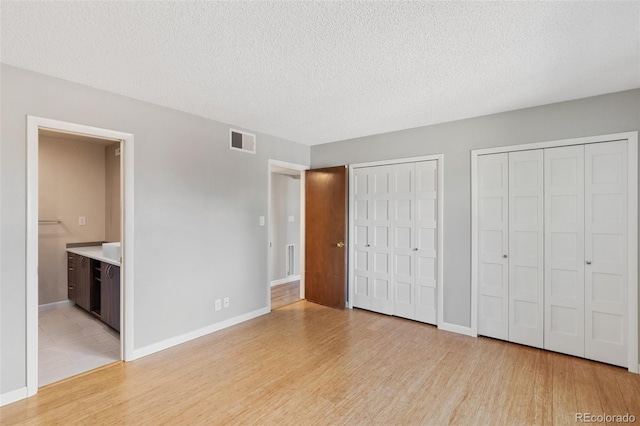 2973 Mesa Rd Unit C, Colorado Springs, CO 80904 - unfurnished bedroom with two closets, light wood-style flooring, connected bathroom, and a textured ceiling