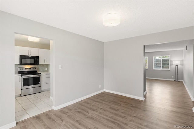 2973 Mesa Rd Unit C, Colorado Springs, CO 80904 - kitchen with electric range, light wood-style flooring, black microwave, white cabinetry, and tasteful backsplash
