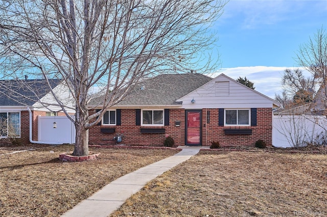 view of front of home featuring a shingled roof, a front yard, brick siding, and fence