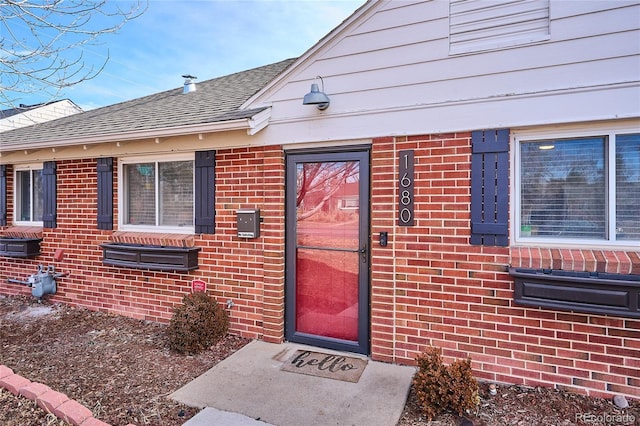 view of exterior entry with brick siding and a shingled roof