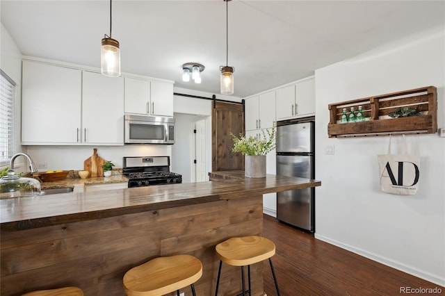 kitchen featuring a barn door, appliances with stainless steel finishes, a peninsula, white cabinetry, and a sink