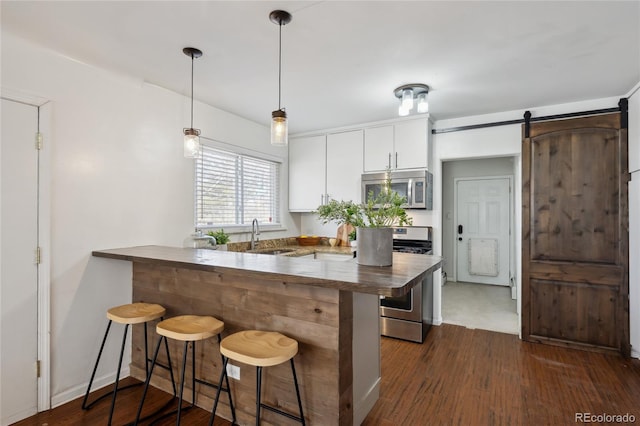 kitchen featuring a barn door, a peninsula, a breakfast bar, white cabinets, and appliances with stainless steel finishes