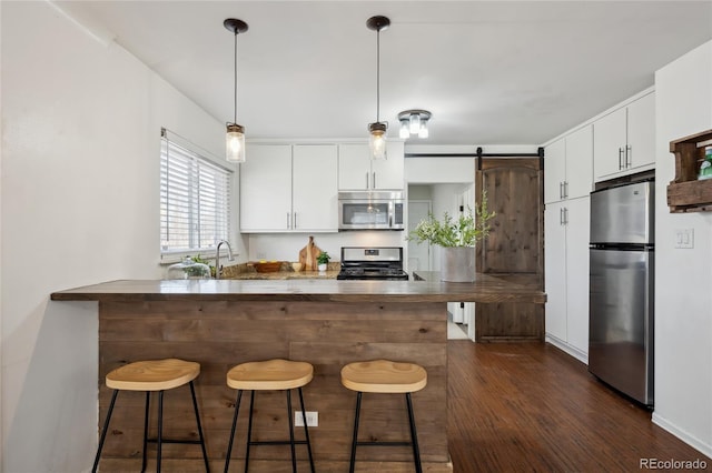 kitchen featuring stainless steel appliances, white cabinets, a breakfast bar area, and a barn door