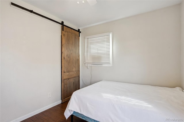 bedroom with a ceiling fan, dark wood-style flooring, baseboards, and a barn door