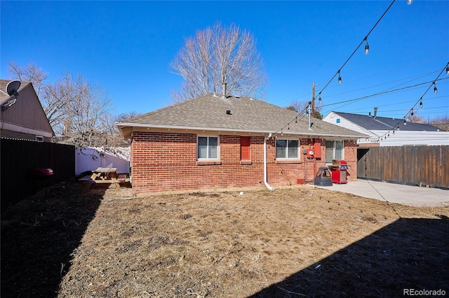 back of property featuring brick siding, a patio area, a fenced backyard, and a shingled roof