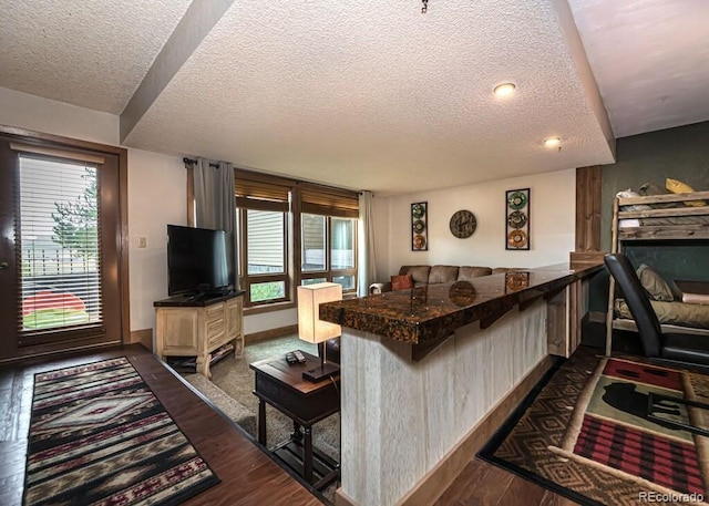 kitchen with a kitchen bar, kitchen peninsula, a textured ceiling, and dark hardwood / wood-style floors