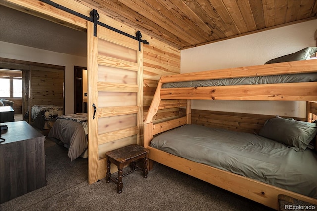 bedroom with dark colored carpet, wood walls, and a barn door