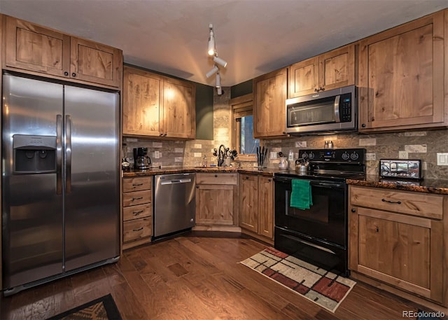 kitchen with dark wood-type flooring, dark stone counters, sink, decorative backsplash, and stainless steel appliances