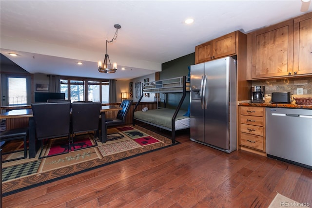 kitchen featuring backsplash, dark stone counters, appliances with stainless steel finishes, dark hardwood / wood-style flooring, and a chandelier