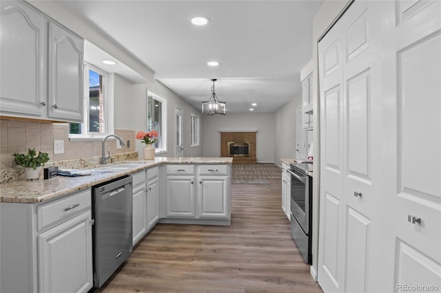 6240 W 110th Pl, Westminster, CO 80020 - kitchen featuring appliances with stainless steel finishes, a brick fireplace, wood finished floors, a peninsula, and recessed lighting