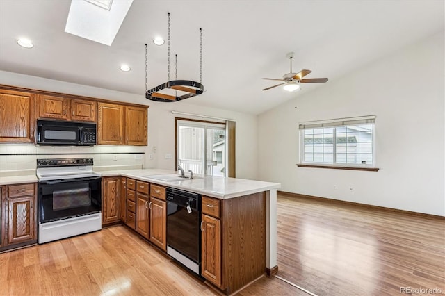 kitchen with vaulted ceiling with skylight, kitchen peninsula, sink, and black appliances