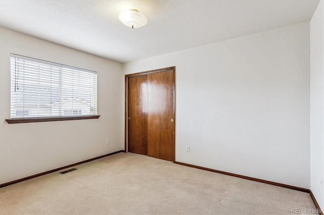 unfurnished bedroom featuring light colored carpet, a closet, and a textured ceiling