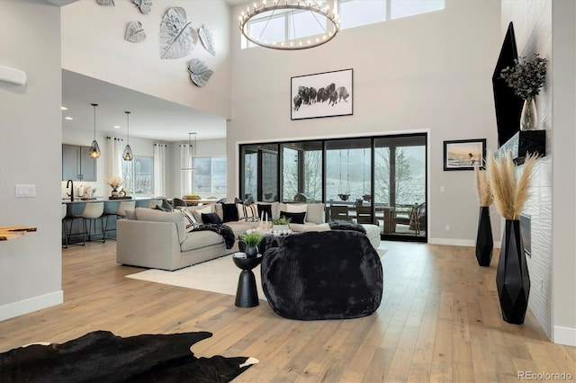 living room featuring a high ceiling, light wood-style floors, baseboards, and a chandelier