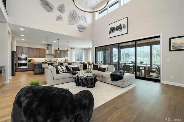 living area featuring baseboards, an inviting chandelier, a high ceiling, recessed lighting, and light wood-type flooring
