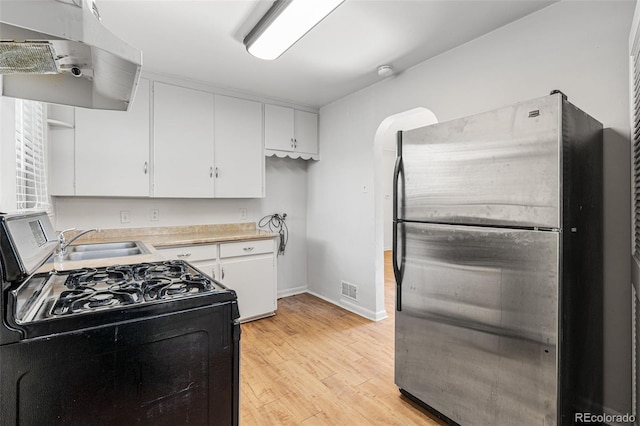 kitchen with stainless steel refrigerator, white cabinets, black range with gas cooktop, and extractor fan