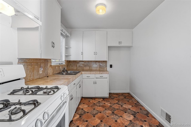 kitchen with white cabinets, white gas stove, decorative backsplash, and sink