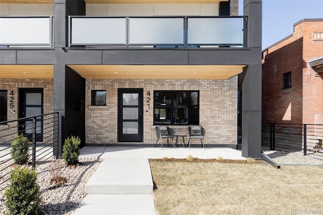 view of exterior entry featuring brick siding, a balcony, and fence