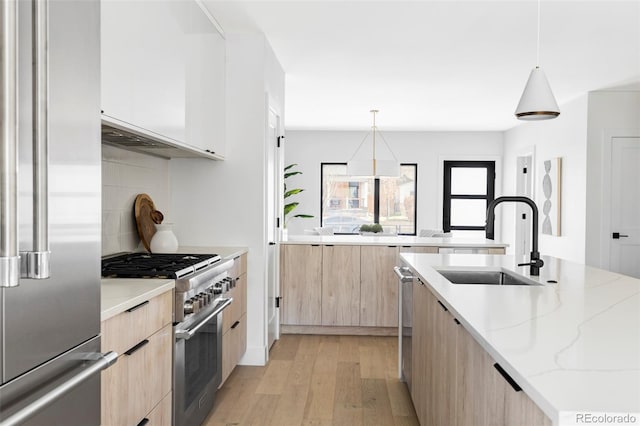 kitchen featuring light stone counters, light brown cabinets, a sink, modern cabinets, and premium appliances