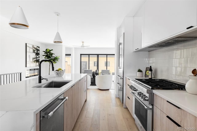 kitchen with modern cabinets, light brown cabinetry, a sink, backsplash, and appliances with stainless steel finishes