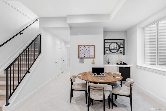 dining space with light carpet, beverage cooler, stairway, baseboards, and bar area