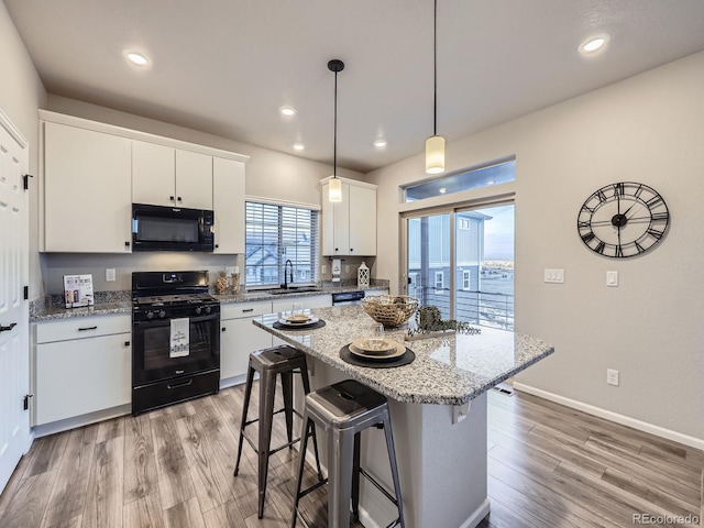 kitchen featuring white cabinetry, a center island, a breakfast bar, black appliances, and pendant lighting