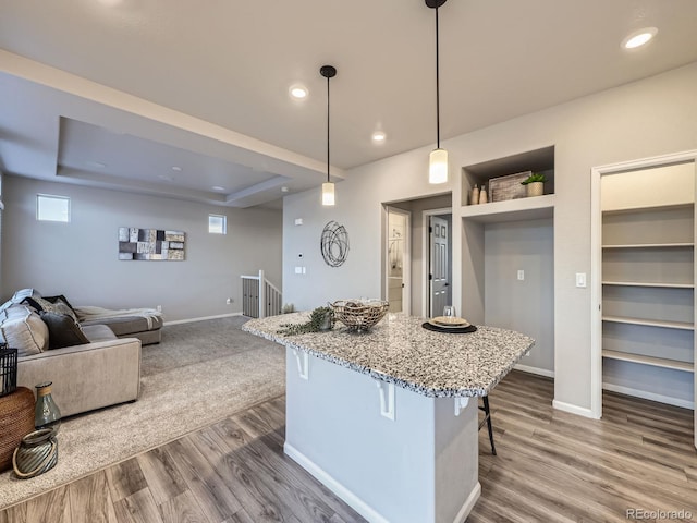 kitchen with a raised ceiling, a kitchen bar, wood-type flooring, hanging light fixtures, and built in shelves