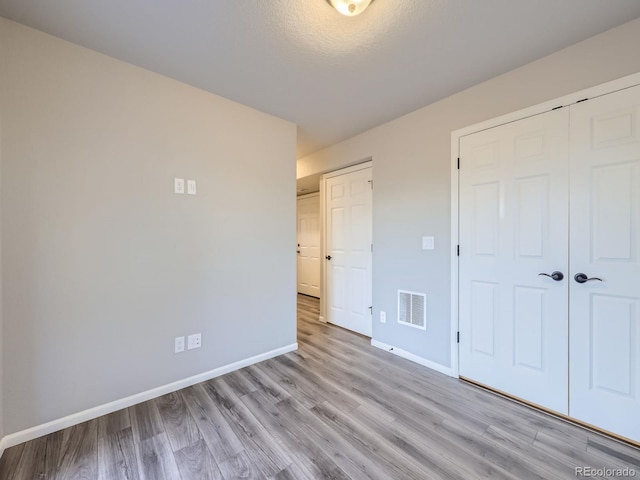 unfurnished bedroom with a textured ceiling, a closet, and light hardwood / wood-style floors