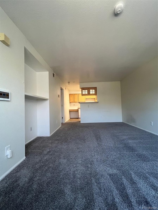 unfurnished living room featuring baseboards, visible vents, dark colored carpet, and a textured ceiling