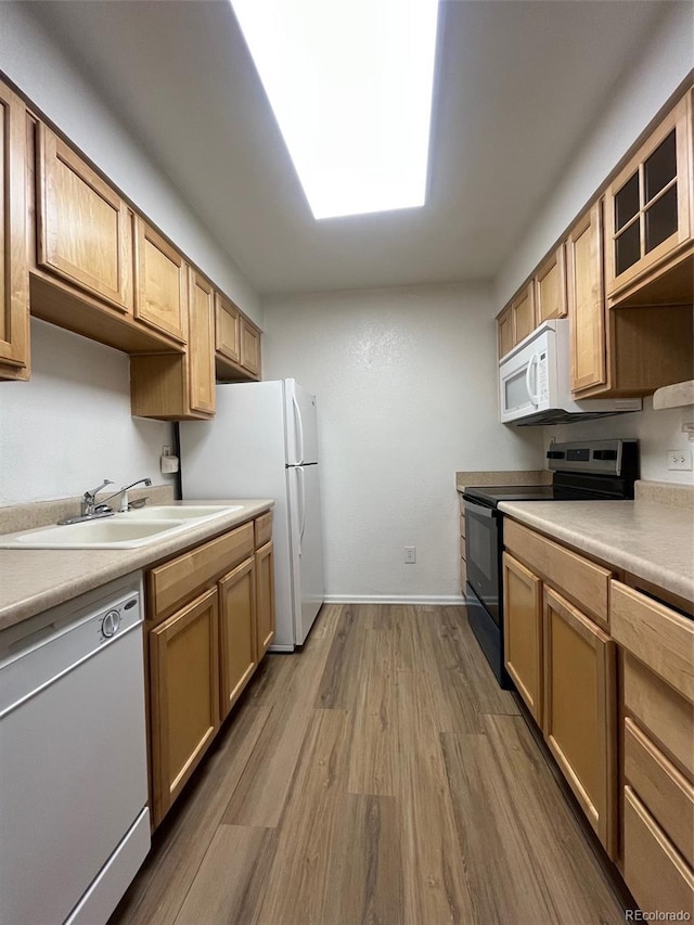 kitchen featuring white appliances, wood finished floors, a sink, baseboards, and light countertops