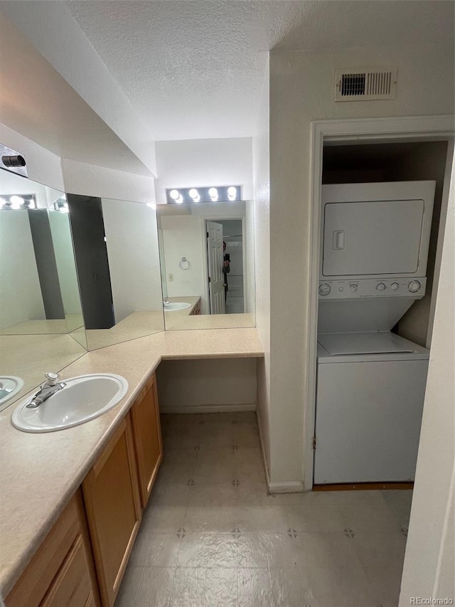 full bathroom featuring stacked washer and dryer, visible vents, a textured ceiling, and vanity