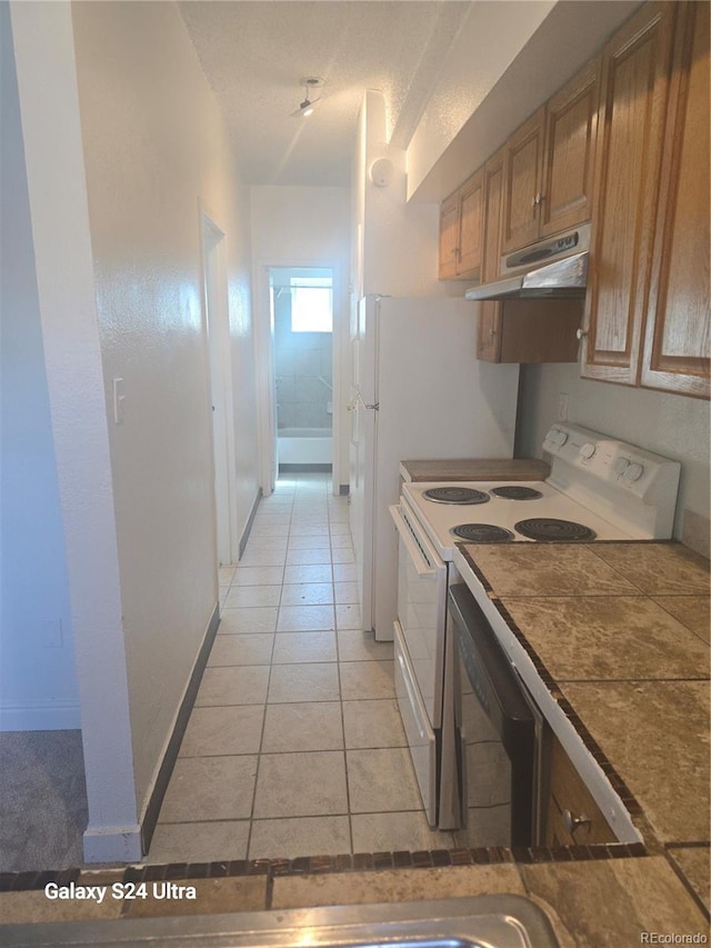 kitchen with white electric stove, brown cabinets, light tile patterned floors, dishwashing machine, and under cabinet range hood