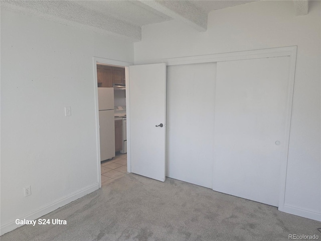 unfurnished bedroom with beam ceiling, a textured ceiling, carpet, freestanding refrigerator, and a closet