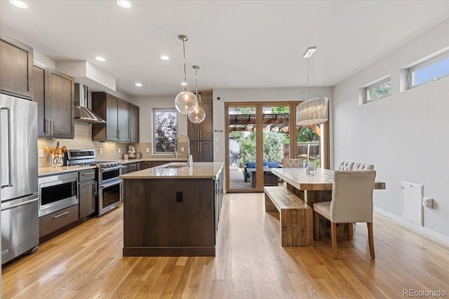 2420 S Gilpin St, Denver, CO 80210 - kitchen with appliances with stainless steel finishes, wall chimney range hood, decorative backsplash, dark brown cabinetry, and a kitchen island with sink