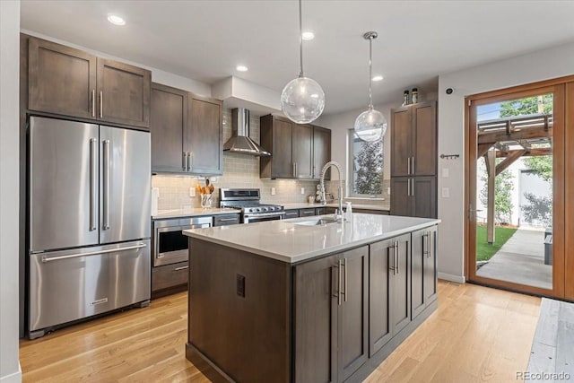 2420 S Gilpin St, Denver, CO 80210 - kitchen featuring appliances with stainless steel finishes, wall chimney range hood, light countertops, light wood-style floors, and dark brown cabinets