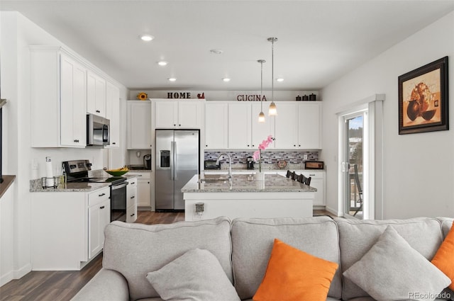 kitchen with appliances with stainless steel finishes, an island with sink, white cabinetry, hanging light fixtures, and light stone countertops