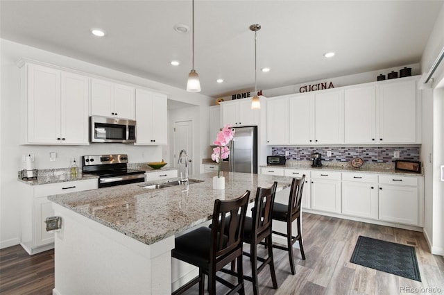 kitchen featuring sink, an island with sink, pendant lighting, stainless steel appliances, and white cabinets