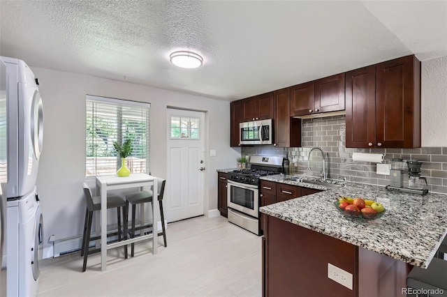 4812 W 8th Ave, Denver, CO 80204 - kitchen with stainless steel appliances, stacked washer and clothes dryer, light stone counters, decorative backsplash, and a peninsula