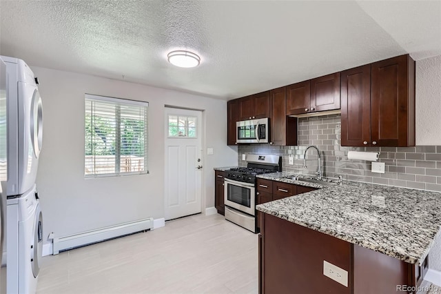 4812 W 8th Ave, Denver, CO 80204 - kitchen featuring stainless steel appliances, a baseboard radiator, stacked washing machine and dryer, backsplash, and light stone counters