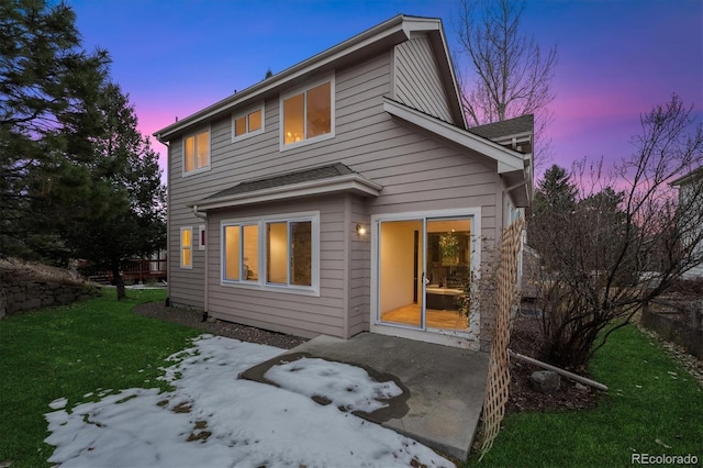 back house at dusk featuring a patio area and a lawn