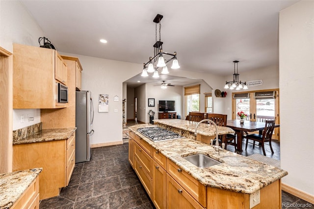 kitchen with ceiling fan, sink, hanging light fixtures, stainless steel appliances, and a kitchen island with sink